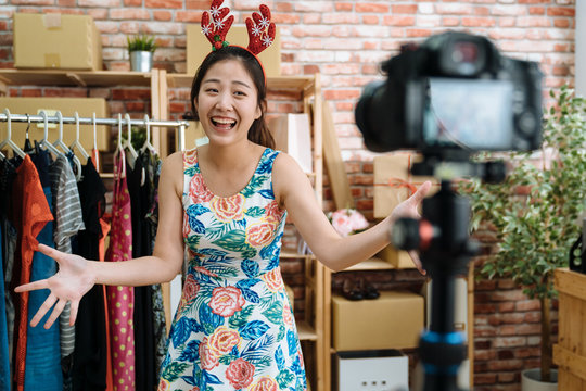 Beautiful Young Asian Girls In Funny Cute Decor Deer On Head With Hands Open Showing Talking To Camera Starting Christmas Holiday Sales In Online Shop Office. Cheerful Woman Live Stream Sell Dresses