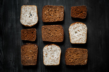 Pattern of wholemeal bread slices on dark wood background. Top view of diverse bread types, low-key image