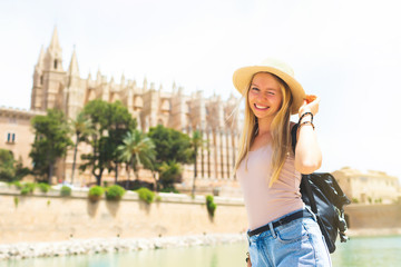 Fototapeta premium Summer hot vacation Europe Spain holiday travel tourism architecture - young beautiful Caucasian walking smiling attractive young girl with hat and backpack in front of the city castle in the city