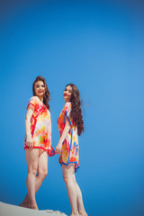 Two gorgeous young women wearing swimmwear, against the blue sky