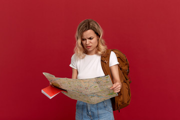 Shocked blond girl with curly hair in a white t-shirt looks at the map trying to find itinerary...