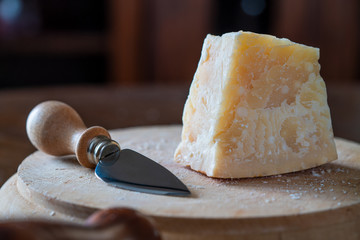 a piece of Italian parmesan on wooden surface with cheese knife closeup