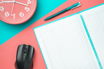 Top view notebook with a pen and a clock and a computer mouse on a colored background