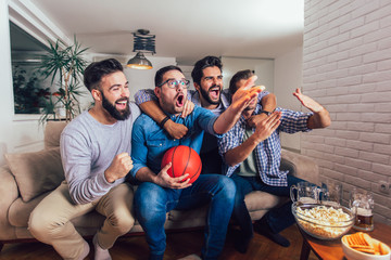 Happy friends or basketball fans watching basketball game on tv and celebrating victory at...
