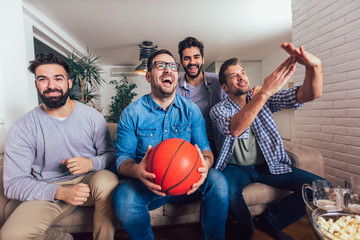 Happy friends or basketball fans watching basketball game on tv and celebrating victory at...