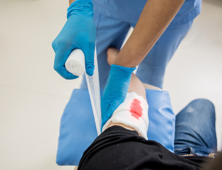 Nurse dressing wound for patient's hand with deep skin cutting.