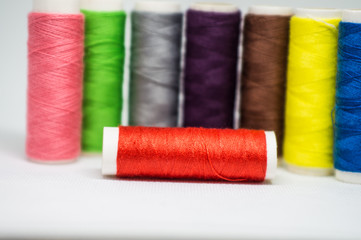 Multi-colored spools of cotton threads for sewing on a white background close-up