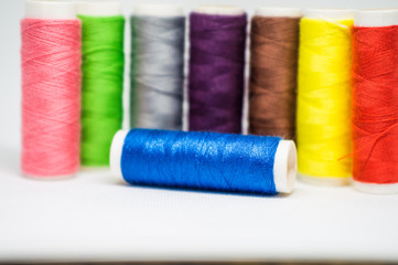 Multi-colored spools of cotton threads for sewing on a white background close-up