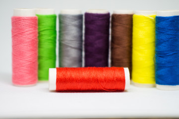 Multi-colored spools of cotton threads for sewing on a white background close-up