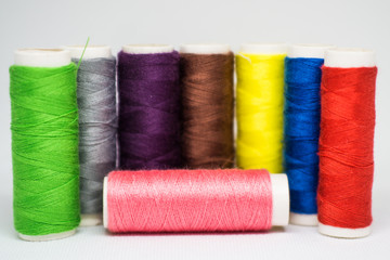 Multi-colored spools of cotton threads for sewing on a white background close-up