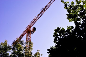 Fototapeta na wymiar Tower crane construction rotary with an arrow on the background of the sky and trees. Lifting machine spatial movement of goods, with the engagement of hook and gripping suspensions.