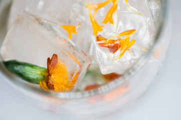 Frozen flower in water in an ice cube, in a transparent glass on a white background close-up.