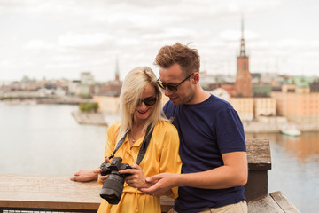 Portrait of the joyful young couple who is standing in the embrace against the background of the city and river and looking at the camera