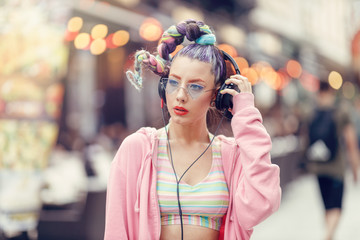 Young girl with crazy avant-garde style listening music in headphones, Urban street style. Outdoor...