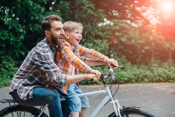 Side view of laughing father with his son on a balance bike. Family having fun together at the green park, daddy teaching son how to ride a bicycle.