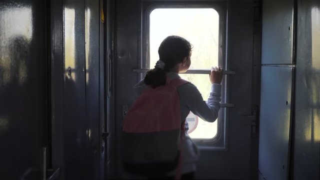 little teenage girl is a backpacker traveling by train. travel transportation railroad concept. tourist school girl in the train lifestyle wagon with backpack looking out the window waving his hand