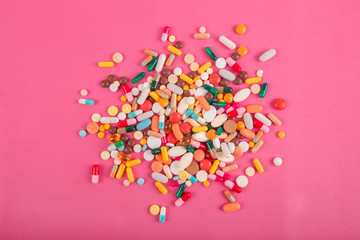 Assorted pharmaceutical medicine pills, tablets and capsules on pink background