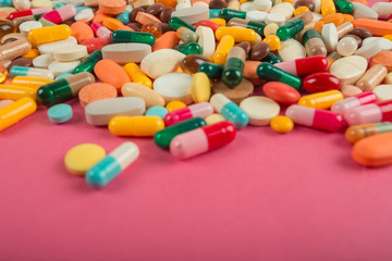 Assorted pharmaceutical medicine pills, tablets and capsules on pink background