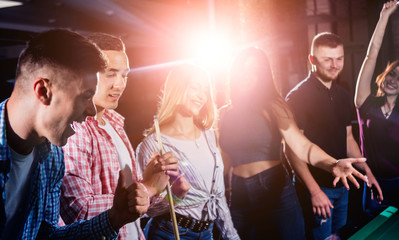 Group of young cheerful friends playing billiards.