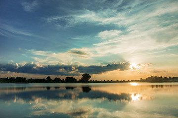 Sun over the horizon, lake and clouds on blue sky