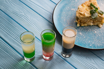 The cocktails and napoleon cake on a blue wooden table.
