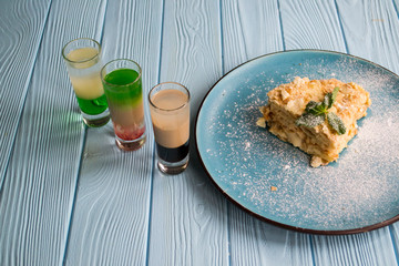 The cocktails and napoleon cake on a blue wooden table.