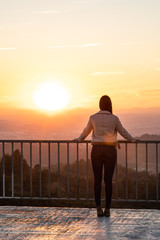 Beautiful woman back shot on a viewpoint railing during sunset with blurred background