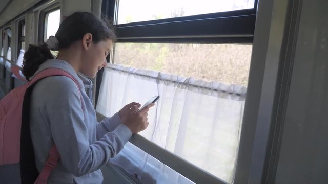 girl teenager traveler with backpack stands by the window of the train car with a smartphone lifestyle. travel transportation railroad concept. the girl in the train at the window corresponds the girl