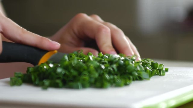 Cutting fresh green onion chives on a small cutting board with a broken knife