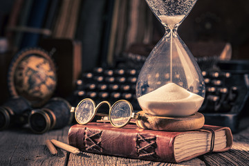Aged journal and hourglass with binocular, compass and books - obrazy, fototapety, plakaty