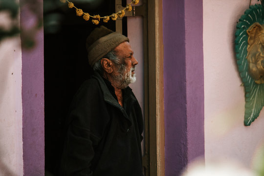 Old Man Wearing Woolen Hat Standing Besides The Door Looking Sideways