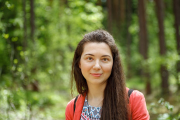 Young attractive smiling woman portrait in red jacket in spring forest among trees