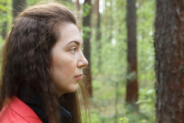 Young attractive woman portrait in red jacket in spring forest among trees