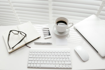 White office desk table with blank notebook, computer keyboard and other office supplies. Top view.