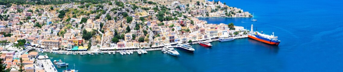 Panoramic view of beautiful bay with colorful houses on the hillside of Symi island in Greece. View on Greek sea Symi island harbor with ships, yachts and houses on island hills