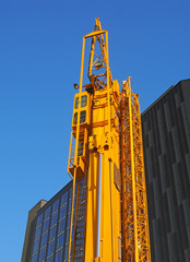 Fototapeta na wymiar a folded yellow construction crane with gantry strapped to the side waiting to be deployed on an urban building site