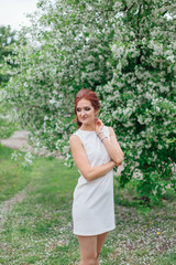 Naklejka na ściany i meble Charming woman wearing beautiful white dress standing under the apple tree