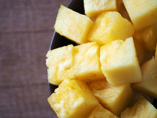 Top view of sliced pineapple chunks in a dark bowl on a wooden table.