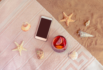 Smartphone and glass of sangria on towel on sand beach. Summer holidays concept.