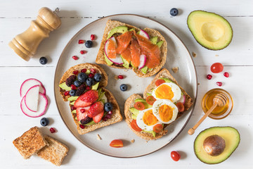 Avocado toast with different topping including salmon fish, eggs, berries, healthy and organic food, breakfast meal on white wooden background