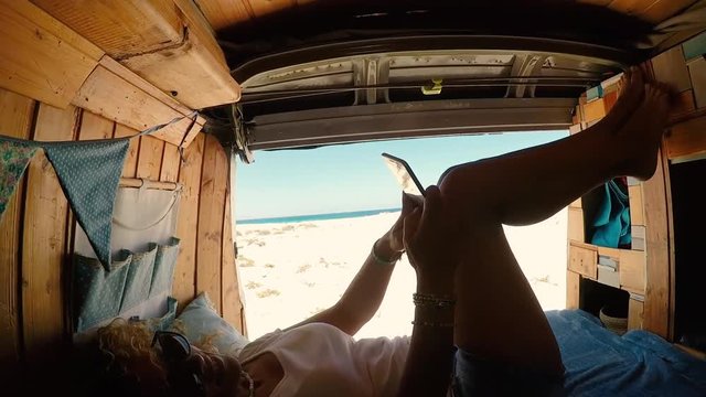 Relaxed alternative trendy woman messaging with the mobile phone inside an old camper van for trendy vacation traveling in tropical places with internet connection always - van life and wanderlust