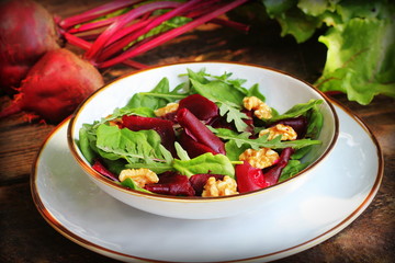 Healthy Beet Salad with fresh sweet baby spinach, arugula, nuts on wooden background