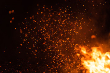 Burning red hot sparks fly from big fire. Beautiful abstract background on the theme of fire. Burning coals, flaming particles flying off against black background.