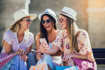 Three girls with colorful shopping bags using smart phones