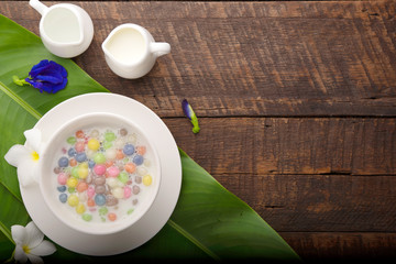 Thai sweets and colorful ball flour in a white cup on a banana leaf, coconut on an old wooden table Rainbow sweets, popular and famous Thai desserts, Bua Loi, Bua Loi, Pandan leaves