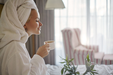 Happy Girl with a Cup of Coffee. Home Style Relaxation Woman Wearing Bathrobe and Towel after...