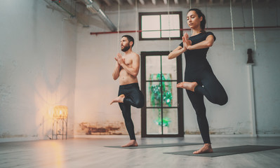 Fototapeta na wymiar Yoga Practice Exercise Class Concept. Young woman and man practicing yoga indoors. Two sporty people doing exercises