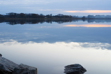 Gray evening sunset above the lake or river. Blue clouds on horizon