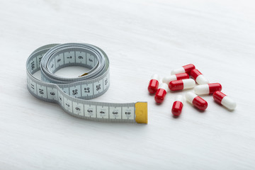 Red and white diet pills lie on a white table next to a measuring tape. Concept of weight loss with...