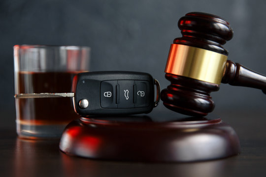 The concept of a DUI. Law hammer, alcohol and car keys on wooden table, dark background